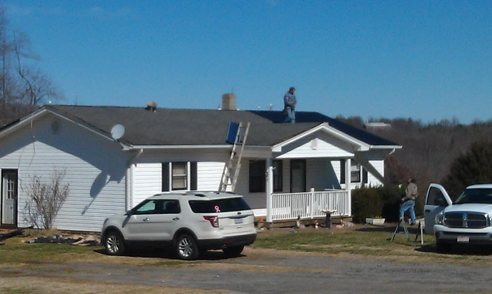 Roofers stripping shingles from a white ranch house roof in Clinton